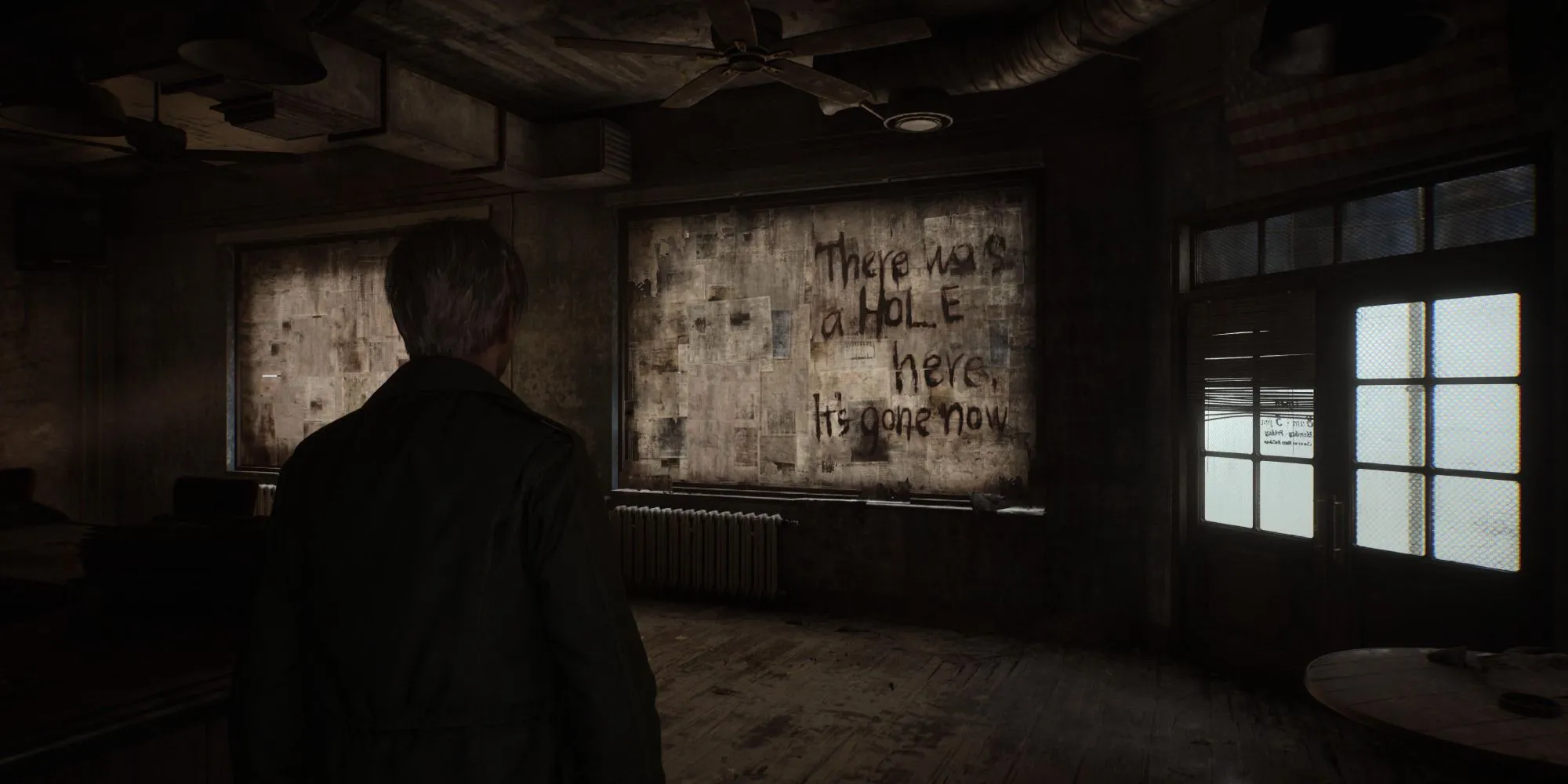 Một cảnh trong Silent Hill 2 Remake cho thấy thông điệp bí ẩn trên tường gần một cái hố, thể hiện không khí kinh dị tâm lý đặc trưng